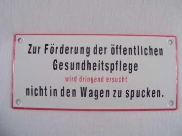 Emailleschild weiß, mit schwarzer Schrift  "Zur Förderung der öffentlichen Gesundheitspflege wird dringend ersucht nicht in den Wagen zu spucken " ca. 17 x 8  cm.